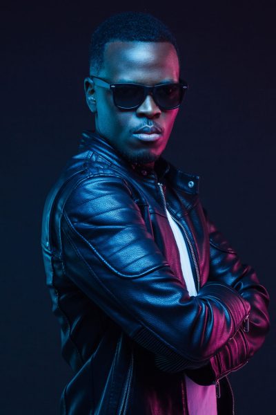 Studio neon portrait of stylish black man standing with crossed arms, wearing leather jacket and sunglasses